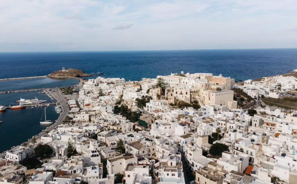 drone view of Naxos Town. the building are painted white and are built all the way up the hill. Temple of Apollo is in the background