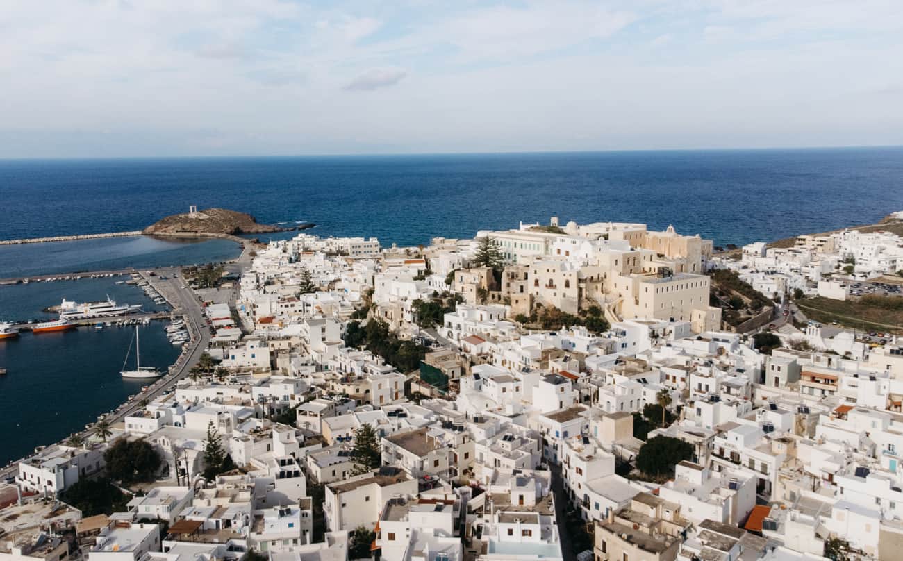 drone view of Naxos Town. Chora is one of the best place to stay in Naxos. the buildings are painted white and are built all the way up the hill. Temple of Apollo is in the background