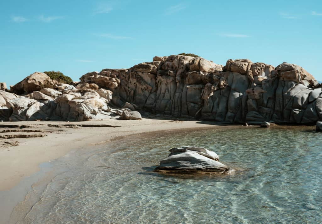 The iconic rock formations at Kolymbithres Beach in Paros, just down the road from Naoussa. There are rocks in the crystal-clear water and a sandy shore below the cliffs.