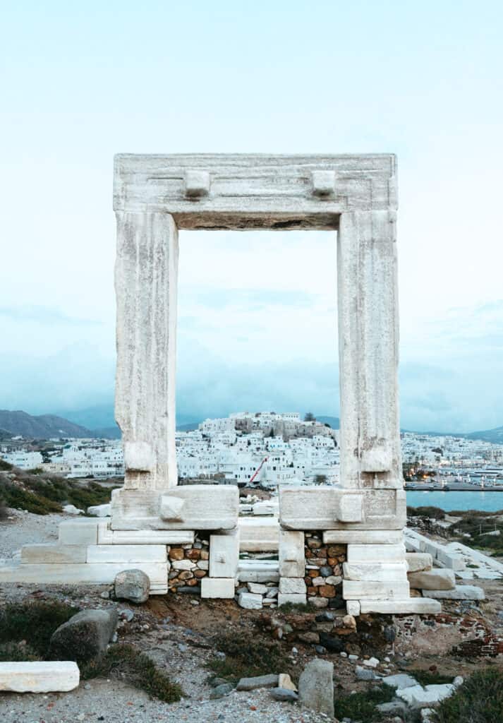 a front view of Portara or Temple of Apollo in Naxos, Greece. The main archway is framing Naxos Port and the main town in the distance