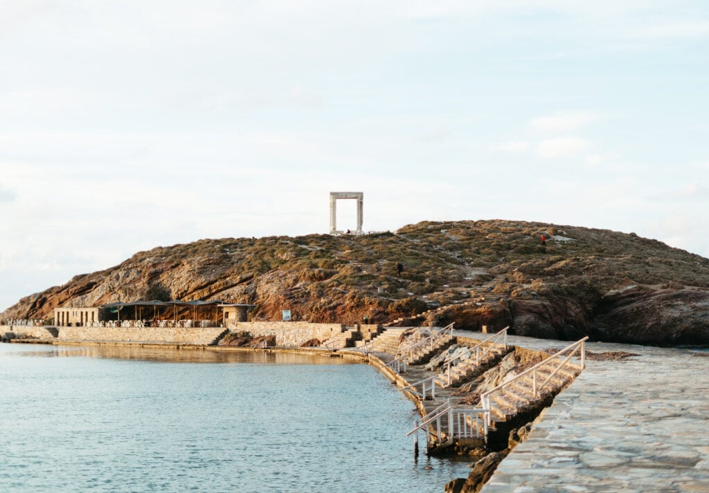 Walking along the stone path at sunset toward Portara or Temple of Apollo in Naxos, Greece.