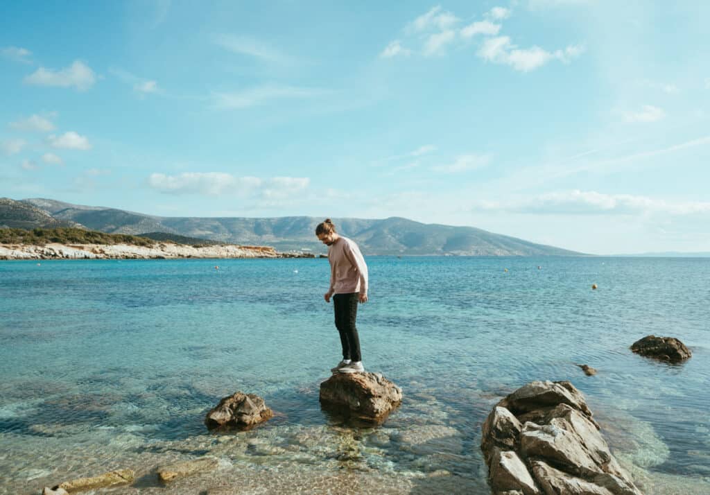 Caleb standing on a rock in the ocean at Alyko Beach, Naxos. The water is incredibly clear and blue
