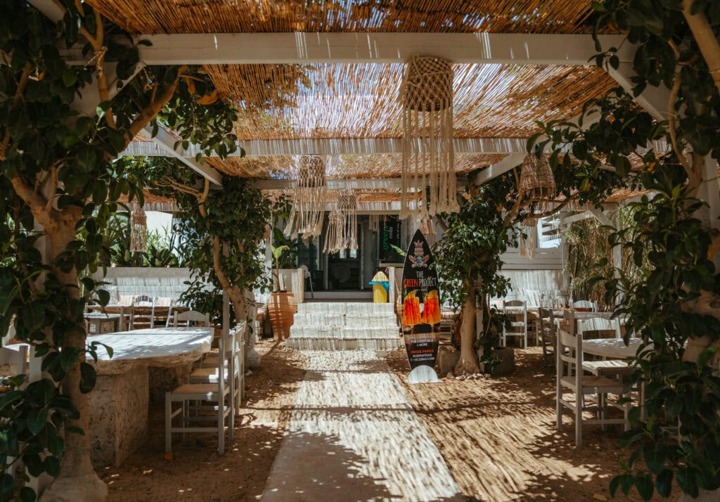 Shaded outdoor dining area at a beachfront restaurant near Golden Beach Paros with rustic decor and greenery.