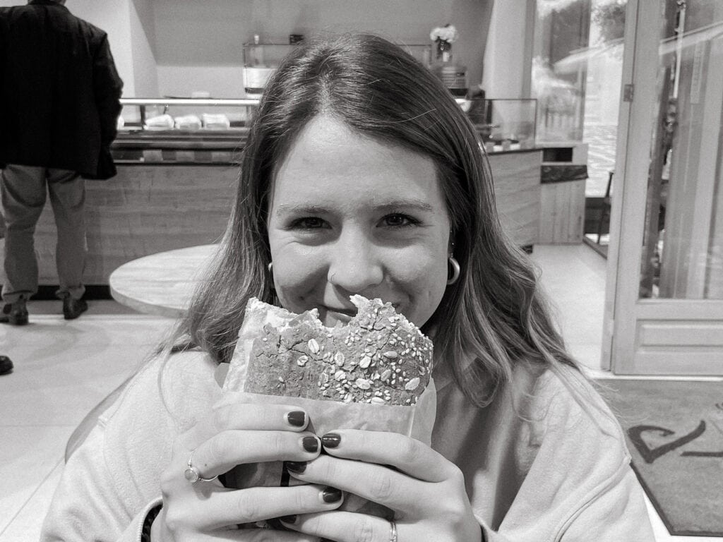 Sarah is about to take a bite of a seeded sandwich in a cozy cafe in Paros, Greece
