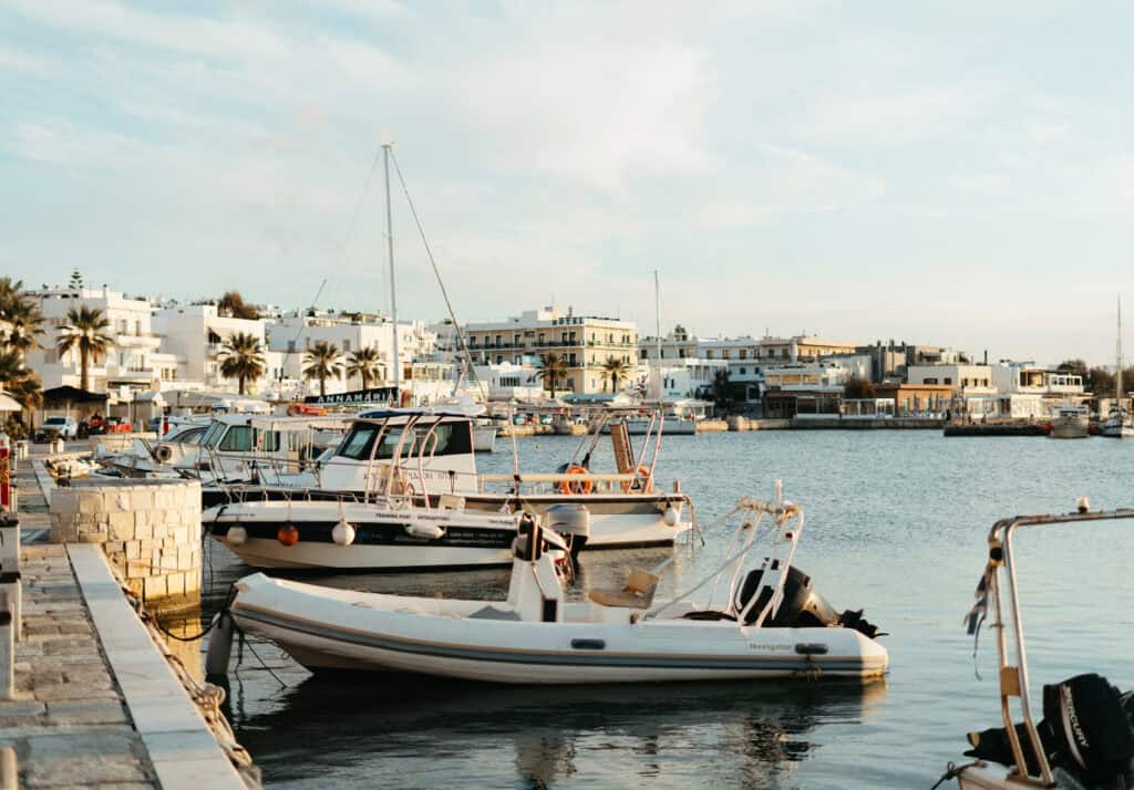 Boats docked in a marina with white buildings and palm trees in the background under a clear sky, capturing a serene coastal town atmosphere.