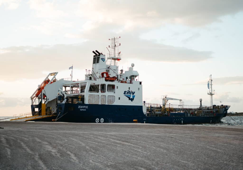 Large ferry named 'ZEFYROS' docked at a port, with the company logo 'ELIN' and other maritime equipment visible, under a partly cloudy sky.