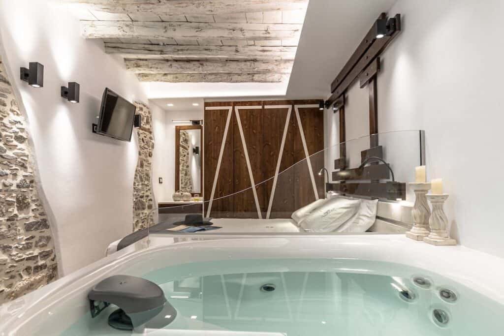 A unique hotel suite featuring a rustic, arched stone ceiling, whitewashed walls, and warm ambient lighting. The cozy setup includes a king-sized bed, a seating area, and vintage-style furniture.
