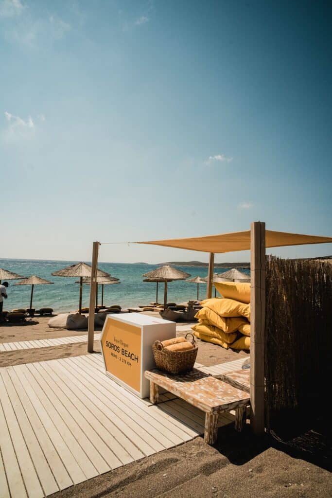 A picturesque beachfront scene with wooden pathways leading to thatched umbrellas and cushioned sun loungers on the sandy shore.