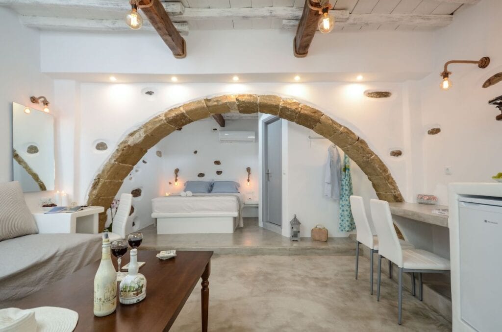 A luxurious spa suite with a large in-room jacuzzi, rustic stone walls, and a barn-style wooden door. Candles and warm lighting create an intimate and tranquil atmosphere.