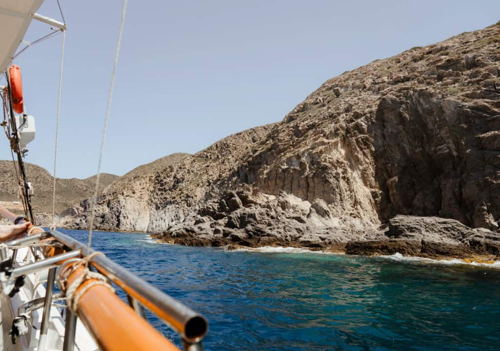 Scenic view of rocky cliffs and crystal-clear water from a sailing vessel during one of our Paros boat tours, showcasing the island's rugged coastline.