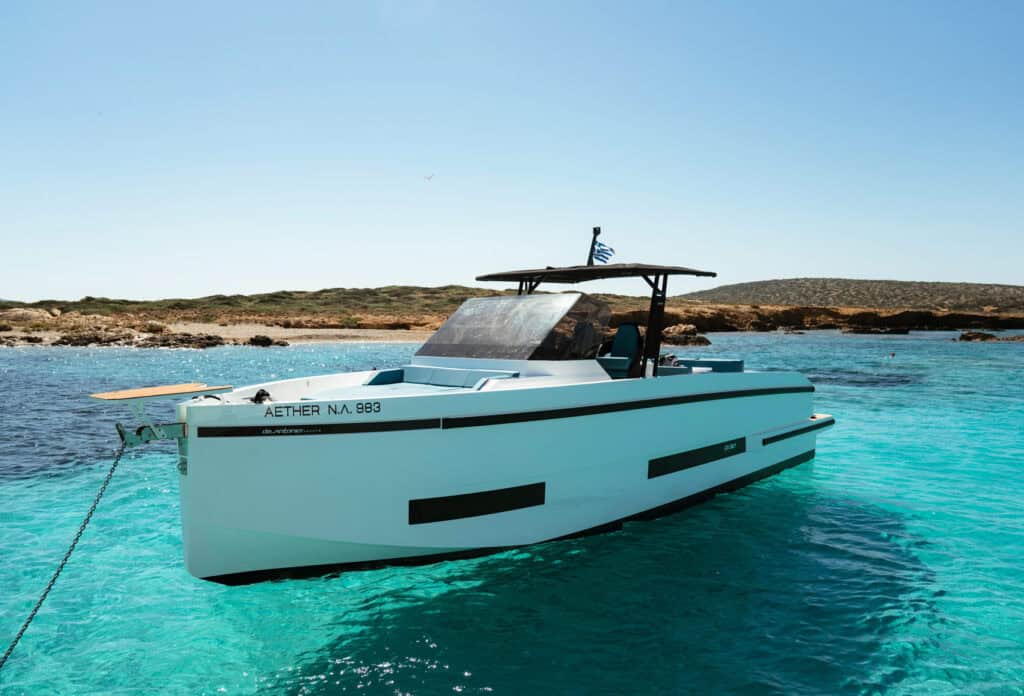 Luxury modern yacht anchored near the shore in shallow, vibrant blue water.