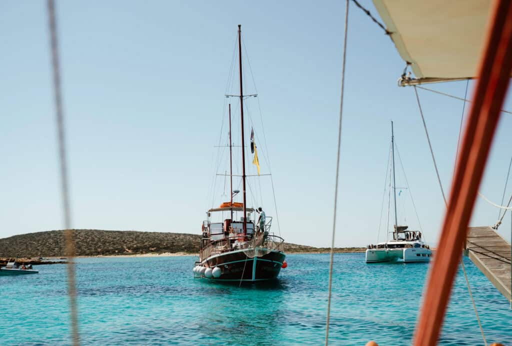 Traditional sailboat anchored in the turquoise Aegean Sea with a catamaran nearby, captured during a relaxing Paros boat tour around the island.