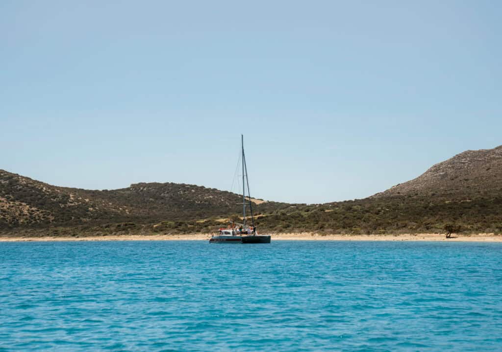 Catamaran floating near a secluded sandy beach and lush hills, a common stop on many boat trips exploring the island’s coastline.