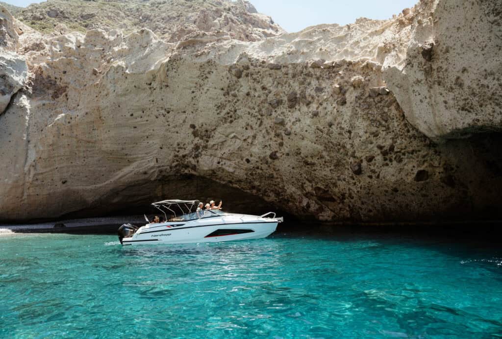 Small white speedboat anchored in a hidden cove with dramatic rock formations and turquoise water.