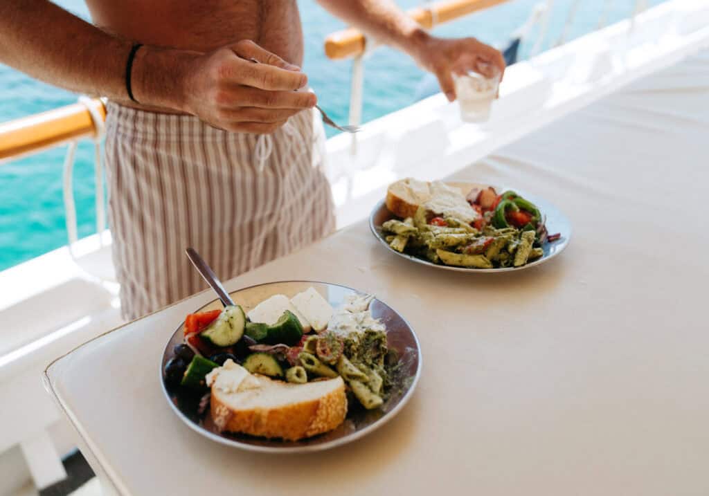 Fresh Mediterranean lunch served on deck during one of the Paros boat trips, featuring pasta, feta, cucumbers, tomatoes, and crusty bread.