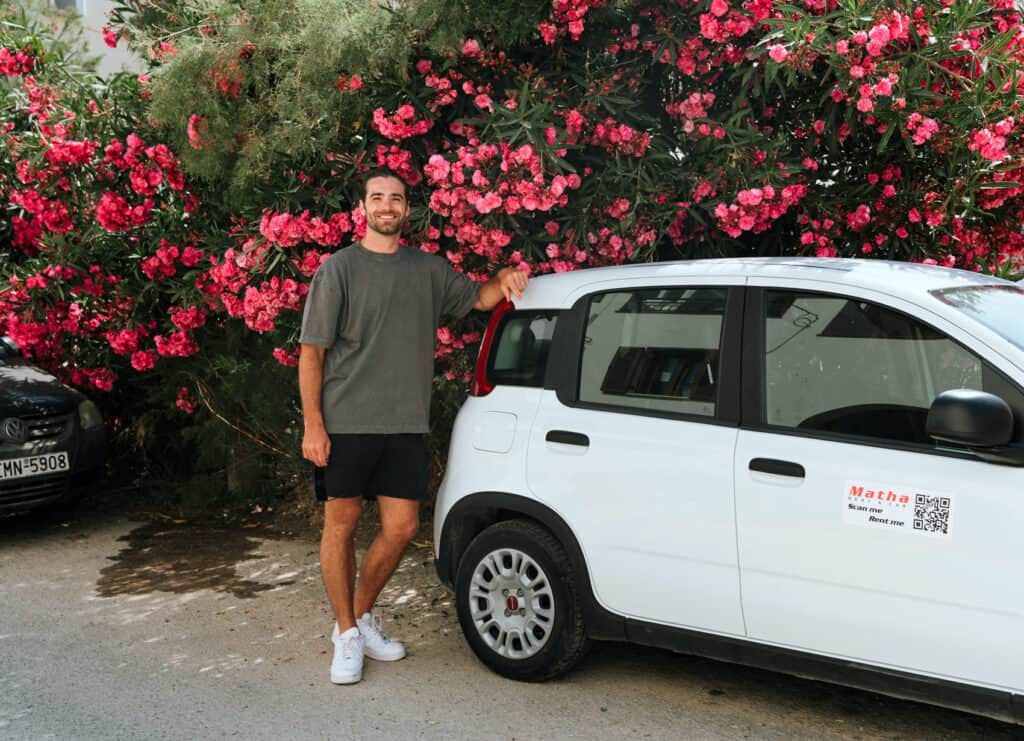 Caleb standing next to our rental car in front of blooming pink flowers after renting a car in Naxos from Matha rental