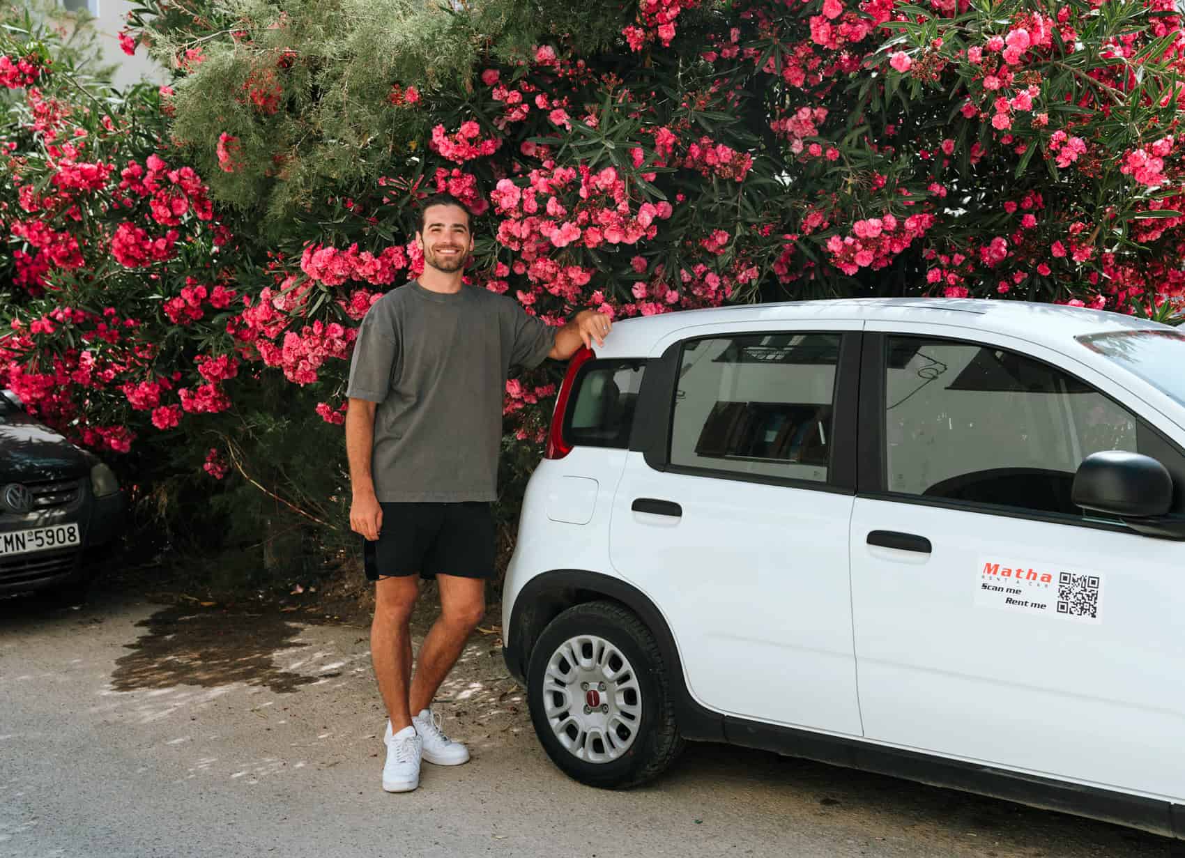 Caleb standing next to our rental car in front of blooming pink flowers after renting a car in Naxos from Matha rental
