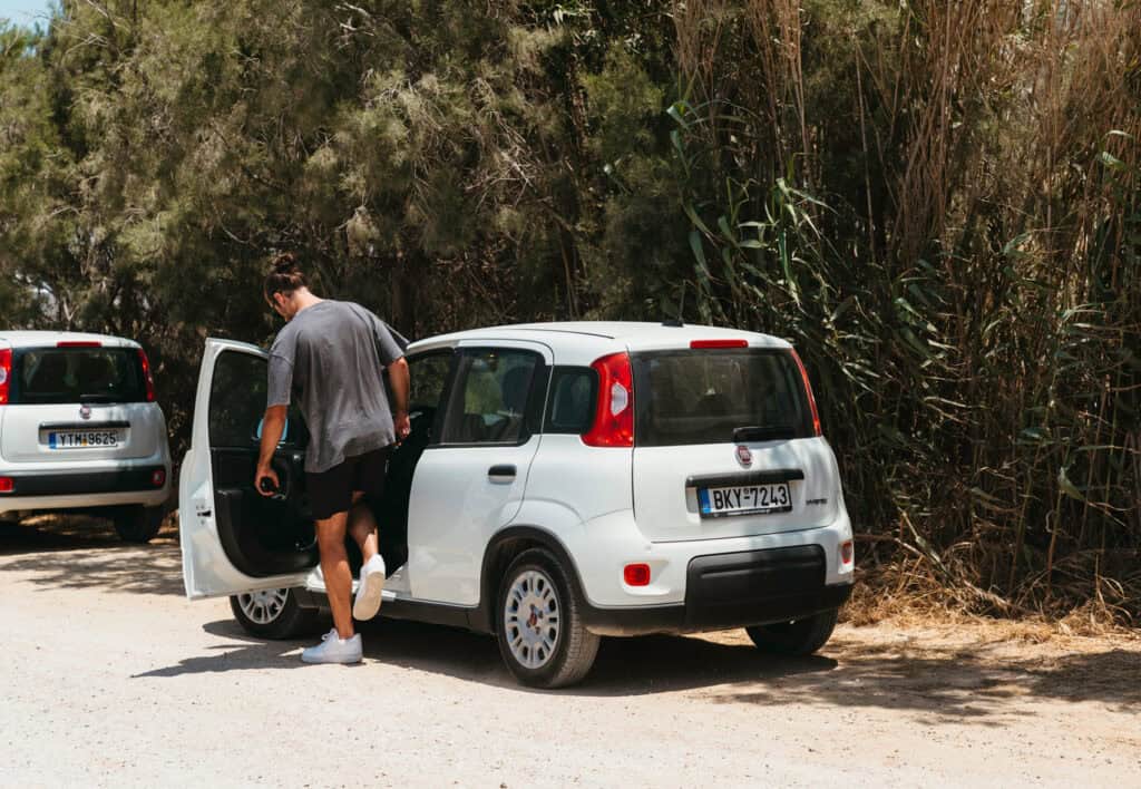 Caleb getting into a white rental car parked on a shaded dirt road in Naxos after renting a car in Naxos