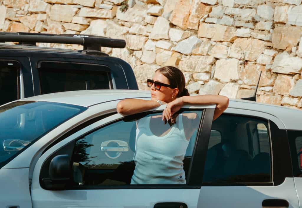 Sarah leaning on the door of a white rental car in Naxos, highlighting the relaxed vibe that comes with renting a car in Naxos