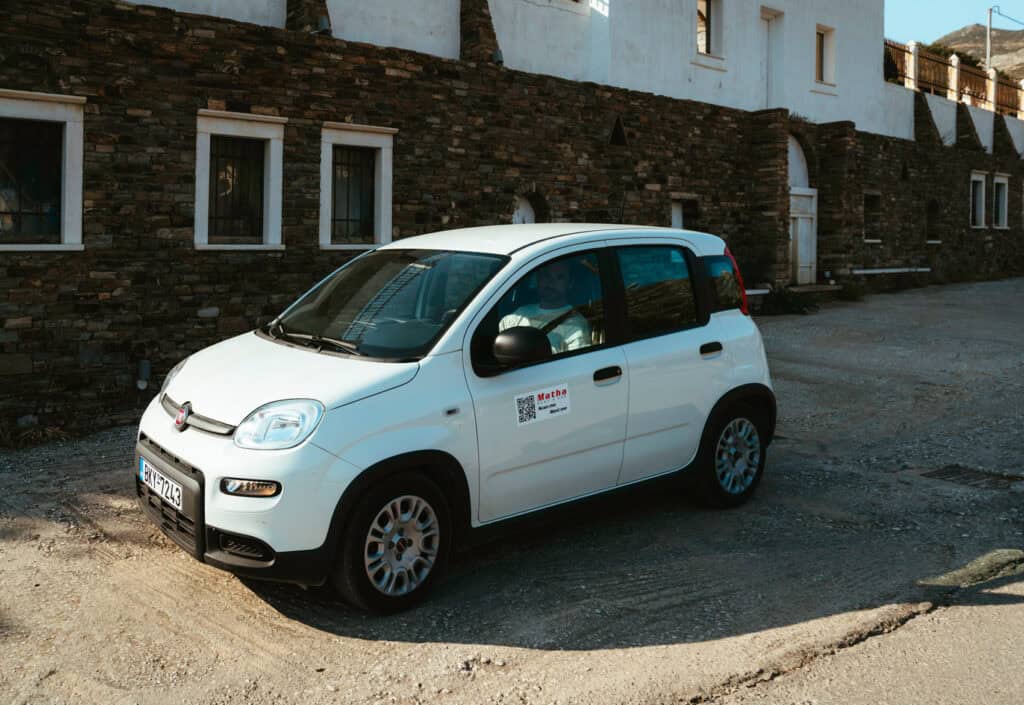 White rental car parked in front of a traditional stone building in Naxos, Greece
