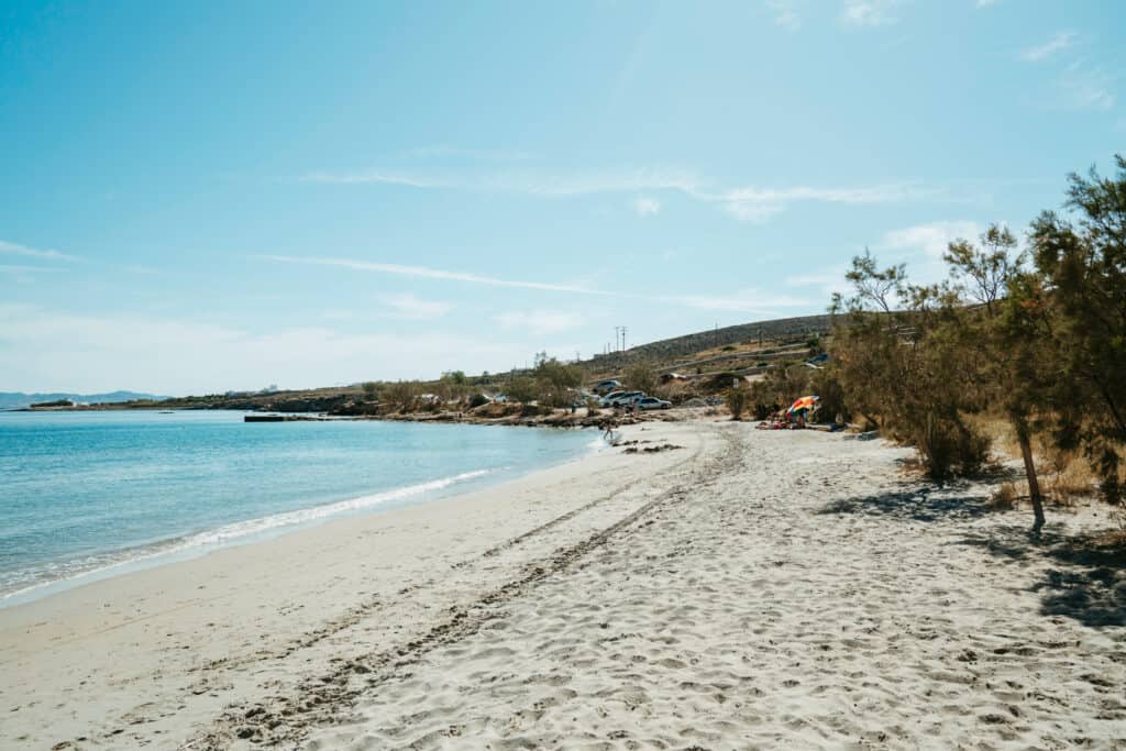Quiet section of Marcello Beach Paros with soft sand, calm blue water, and hillside views, perfect for a peaceful beach day away from the crowds.