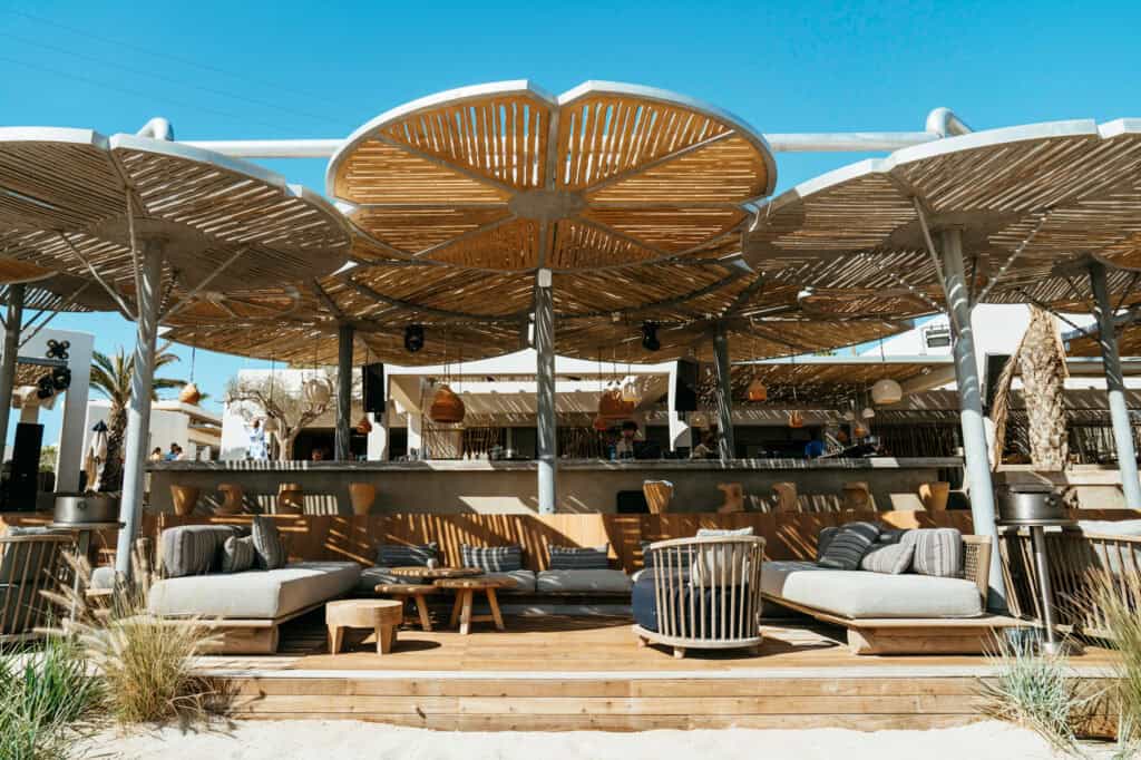 Chic beach bar lounge with wooden umbrellas and modern decor at Marcello Beach Paros, showcasing the upscale, boho atmosphere of the beach’s popular hangout spots.