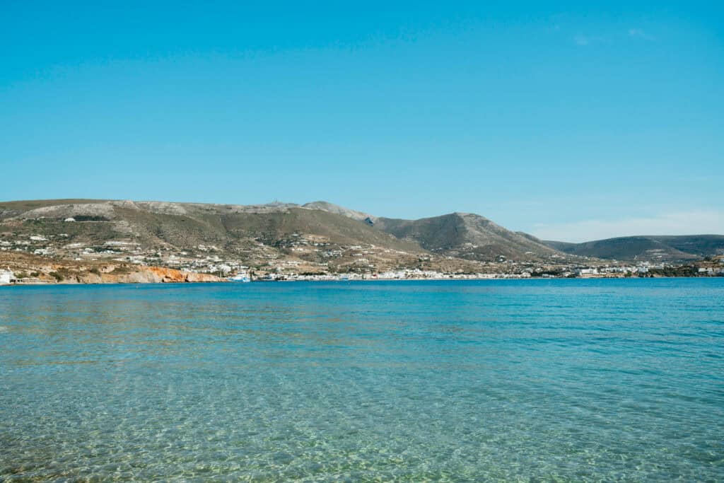 Crystal-clear waters at Marcello Beach Paros with a view across the bay toward the whitewashed buildings and hills of Parikia.