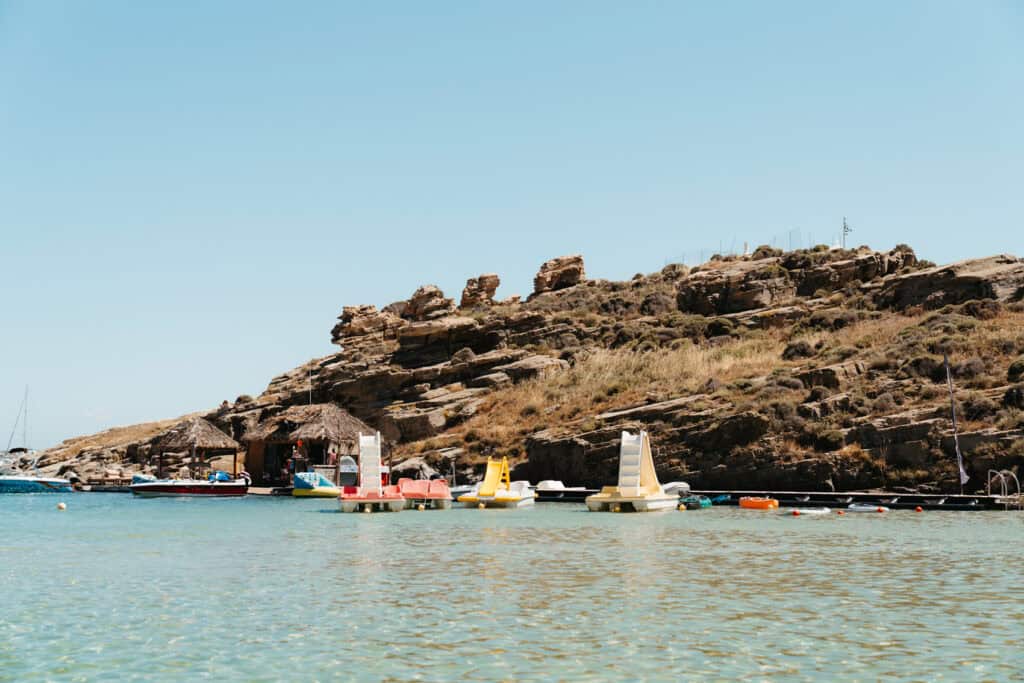 Pedal boats and speedboats docked near a rustic watersports hut at Monastiri Beach, Paros