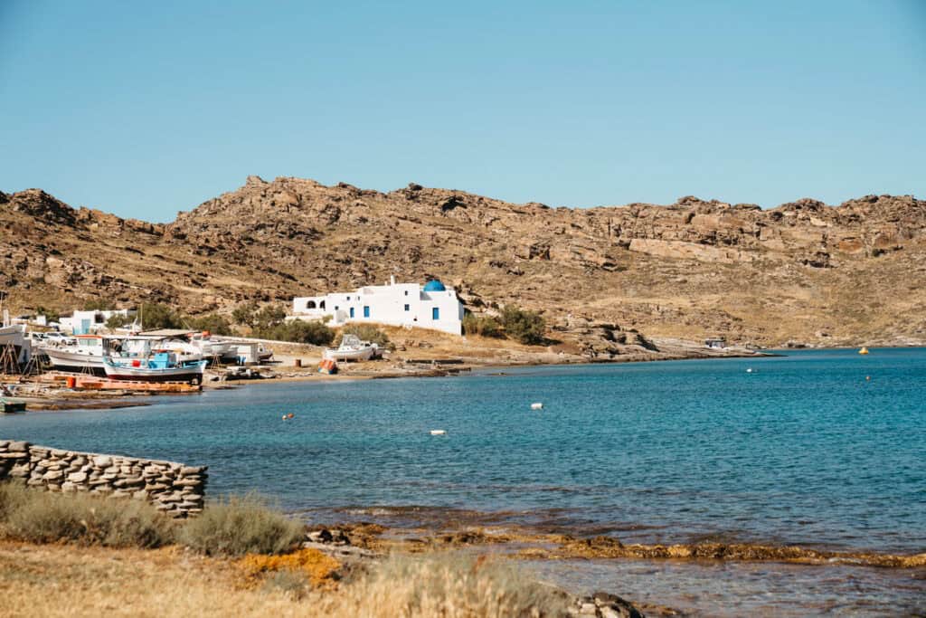 Traditional white church with a blue dome and fishing boats along the shore near Monastiri Beach, Paros