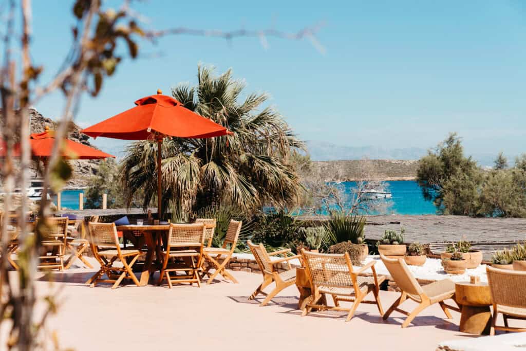 Outdoor seating area at Monastiri Beach Club, Paros, with wooden chairs, red umbrellas, potted plants