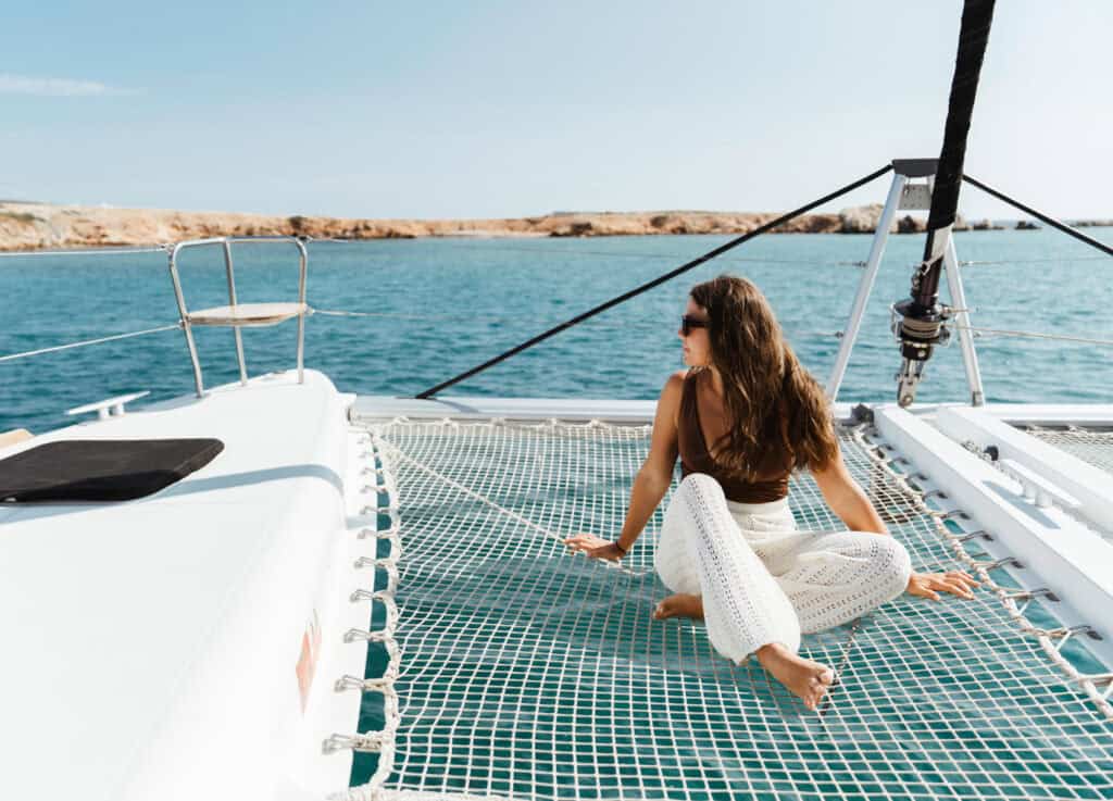 Sarah relaxing on the front net of a catamaran during one of the best boat tours in Naxos, with clear blue water and rocky coastline in the background