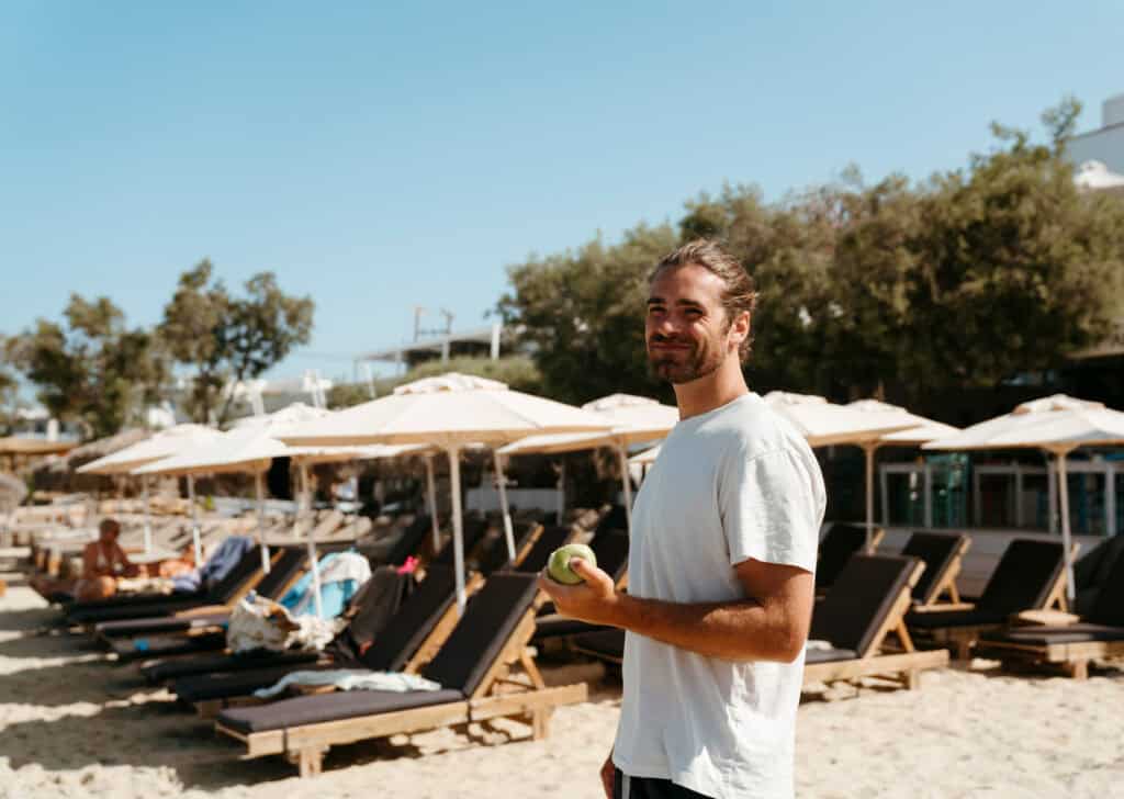 Caleb smiling at the camera on Agia Anna Beach in Naxos, with rows of sun loungers and umbrellas in the background on a sunny day.